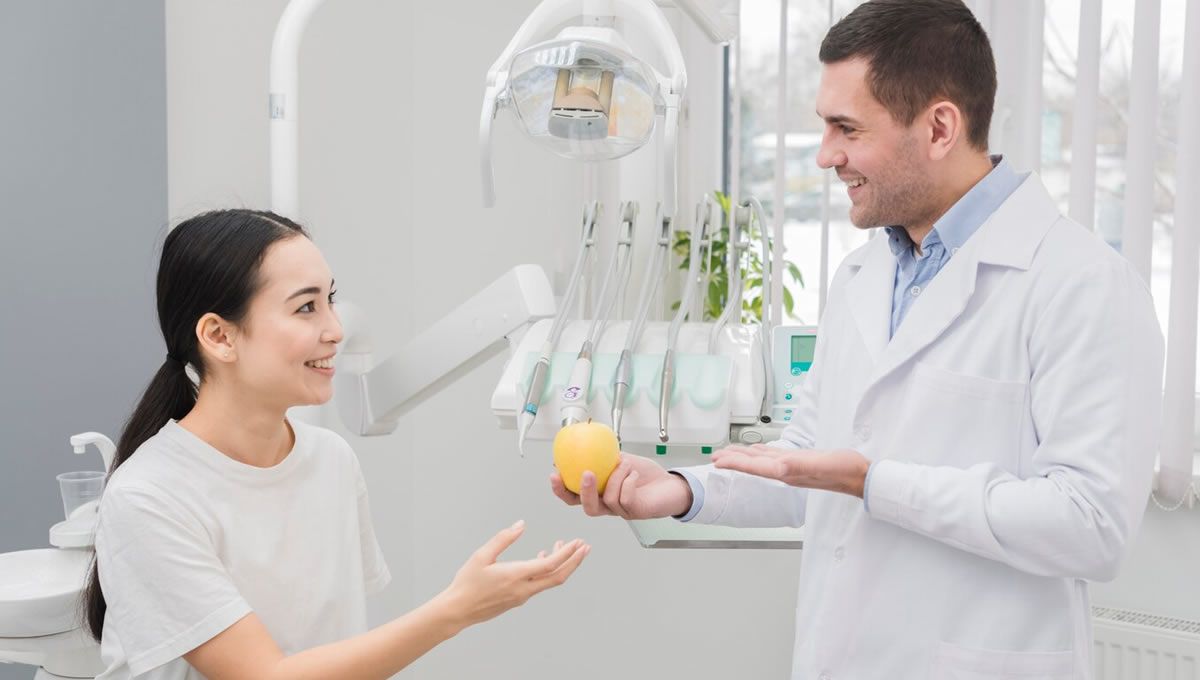 Dentista con paciente en consulta con una manzana (Fuente: Freepik)