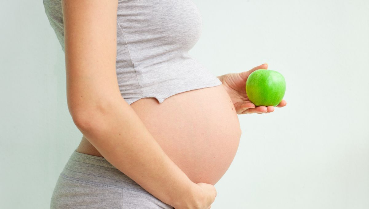 Mujer con embarazo avanzado con una manzana (Fuente: Canva)