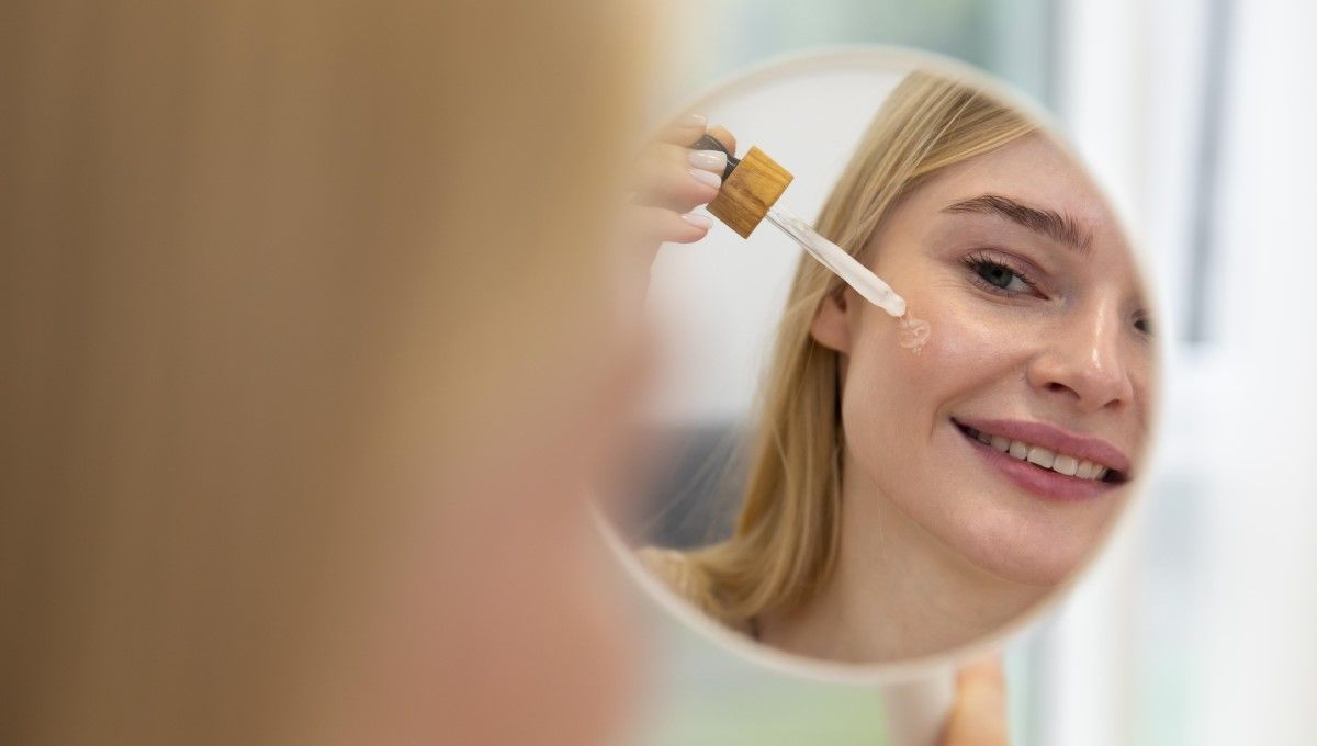 Mujer aplicando un sérum facial frente a su espejo (Foto. Freepik)
