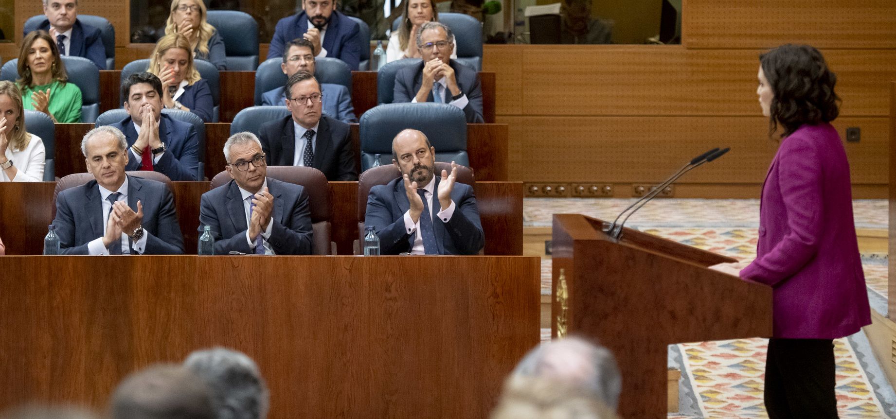 Enrique Ruiz Escudero, sentado a la izquierda en la primera fila, escucha a Isabel Díaz Ayuso (Foto: Flickr PP de Madrid)