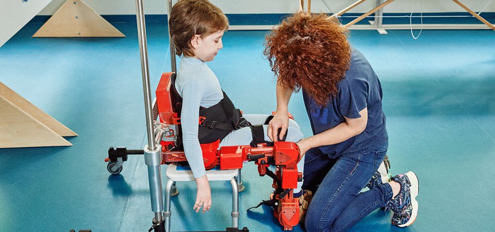 Un niño se enfunda con ayuda de la fisio su exoesqueleto para empezar la terapia (Foto. Marsi Bionics)