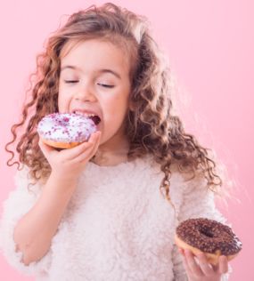 portrait of little curly girl eating donuts