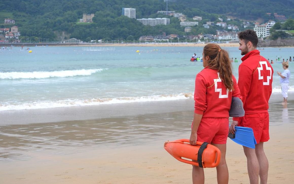 Una pareja de socorristas de la Cruz Roja, atentos ante la actividad de un grupo de bañistas en una playa de la zona norte de España