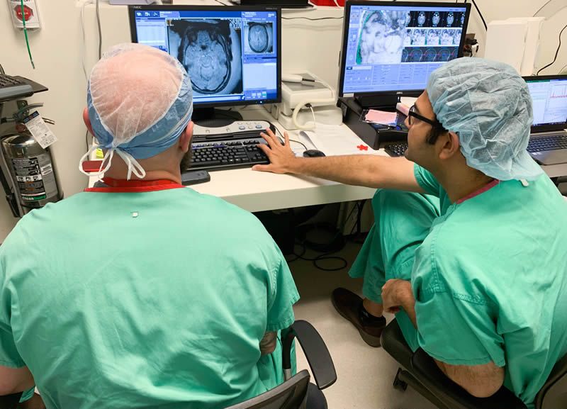 El Dr. Vibhor Krishna (a la derecha) revisa una imagen del cerebro con el técnico de MRI como parte de un nuevo ensayo clínico